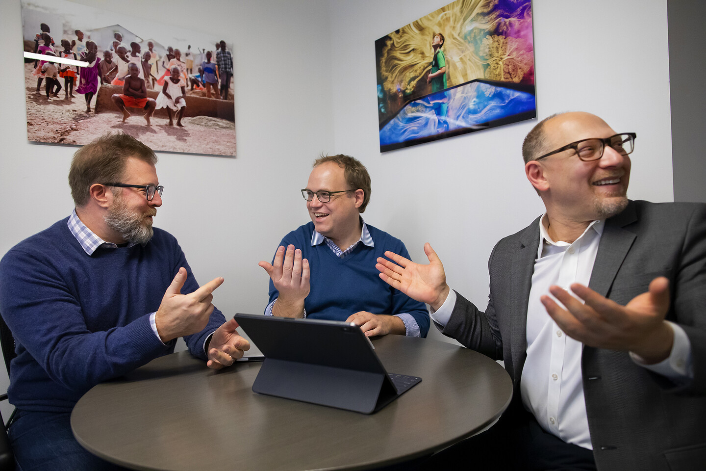 Three people sitting around a table with a laptop computer gesturing and smiling. 