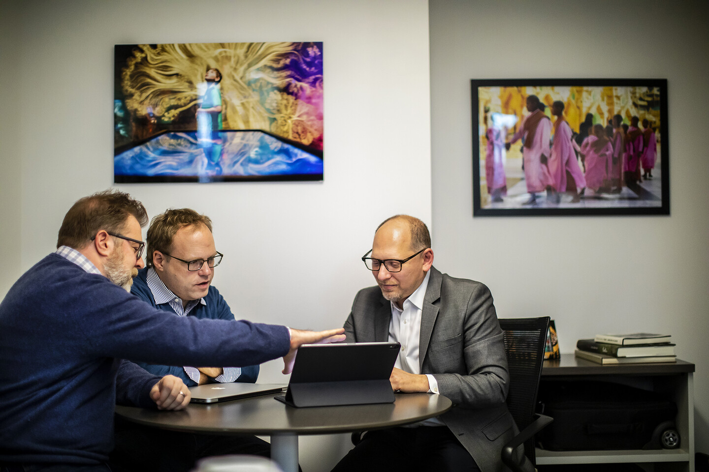 Three people sitting around a table looking at a laptop computer. 