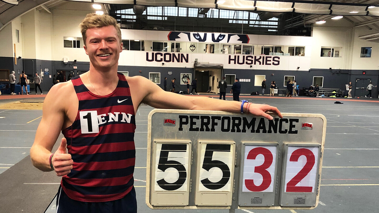 Evan Lee stands next to a scorecard showing his heptathlon while giving the thumps up sign.