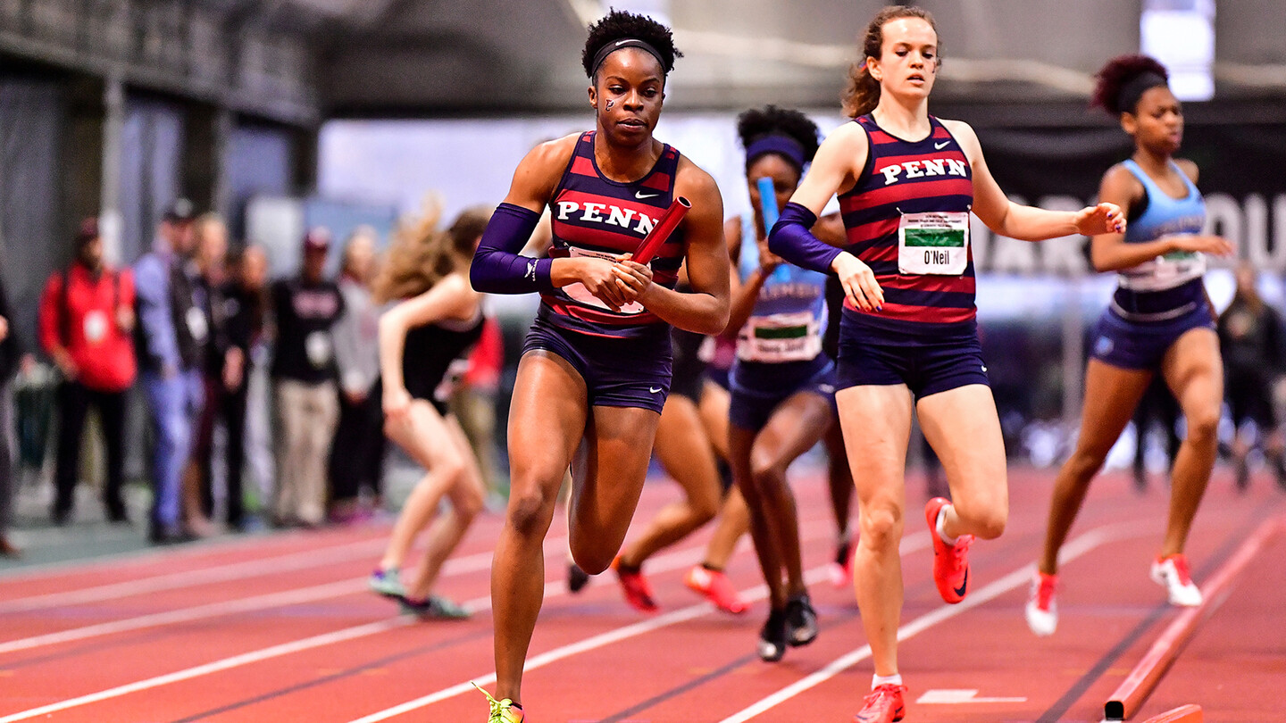 Cecil Ene of the track and field team runs around an indoor track after receiving the relay baton.
