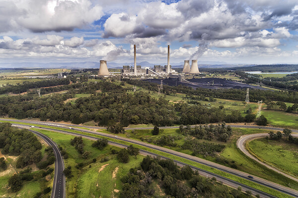 power plant  emitting carbon dioxide into atmosphere on a sunny day, surrounded by trees and roadways..