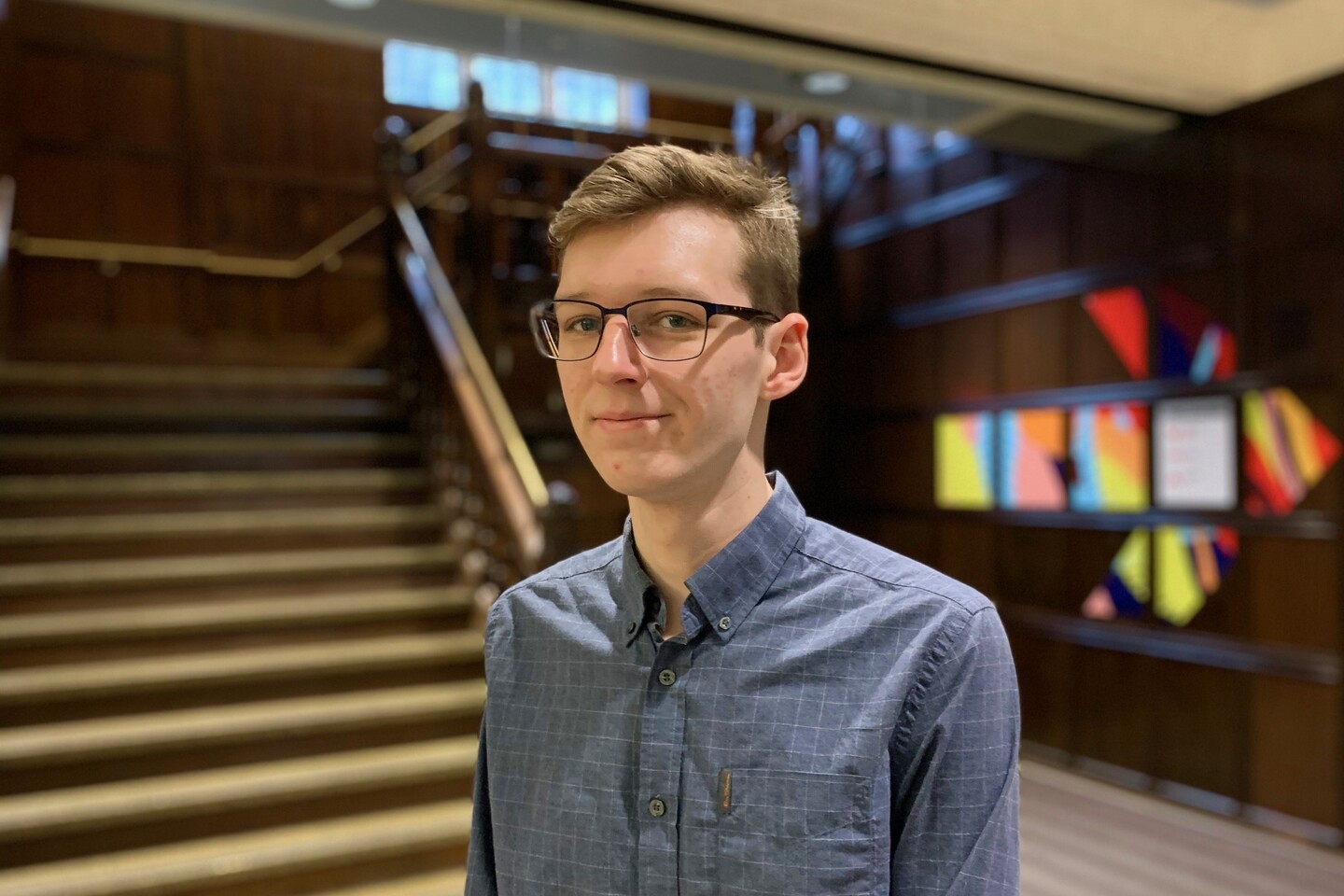 Student standing in lobby with stairs and mural behind