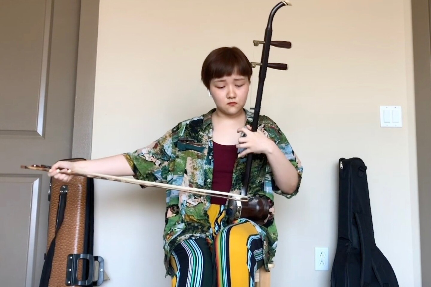 Student sitting playing an instrument held between the knees with two strings played by a bow