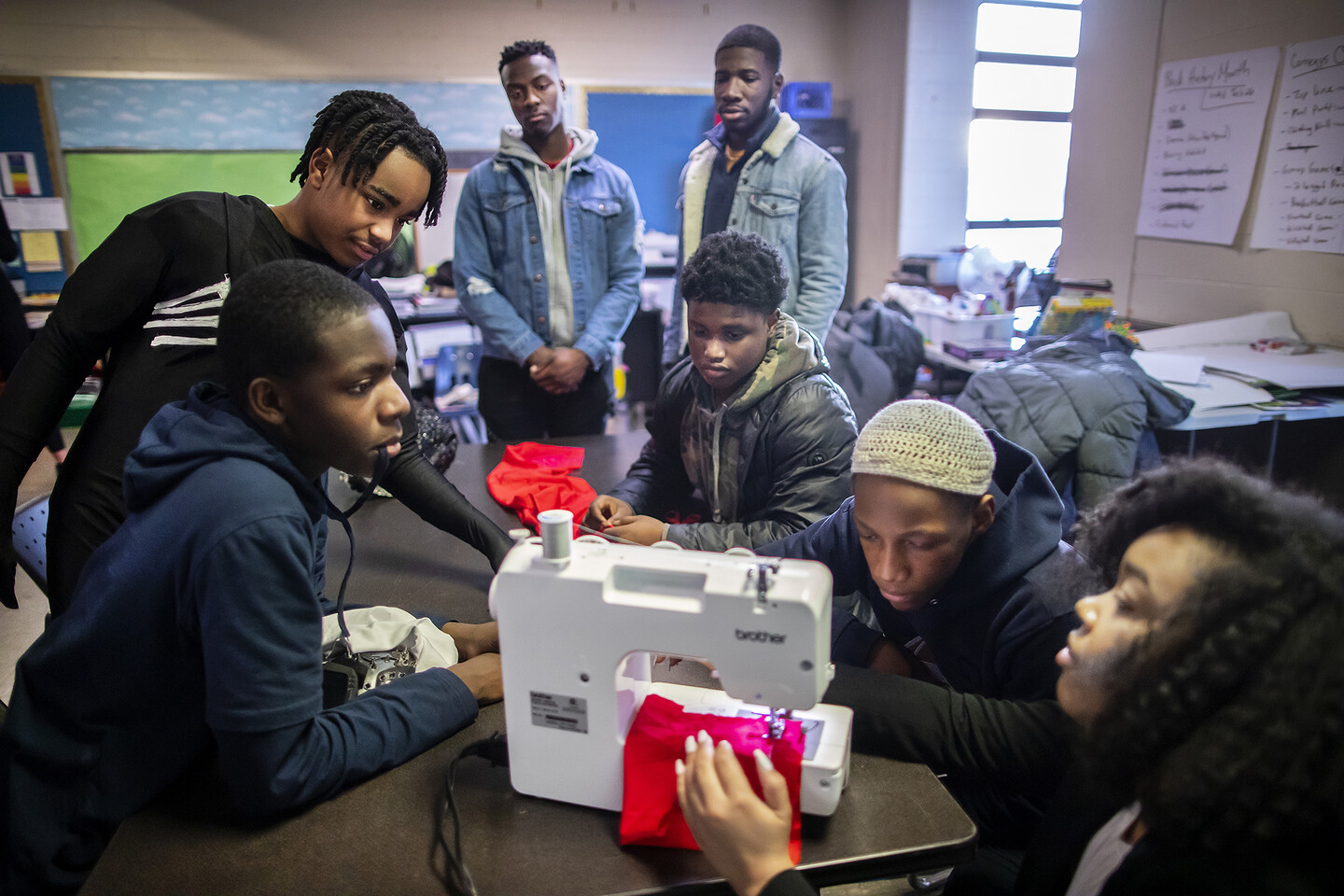 Seven people gather around a sewing machine in a classroom