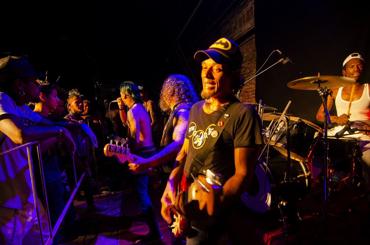 A metal barricade separates the crowd from a guitarist, bassist, drummer, and singer