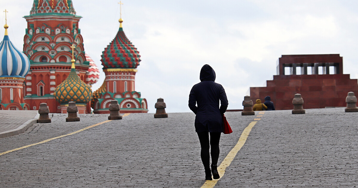Person in black hooded jacket and pants facing away from camera walks near Red Square in Moscow.
