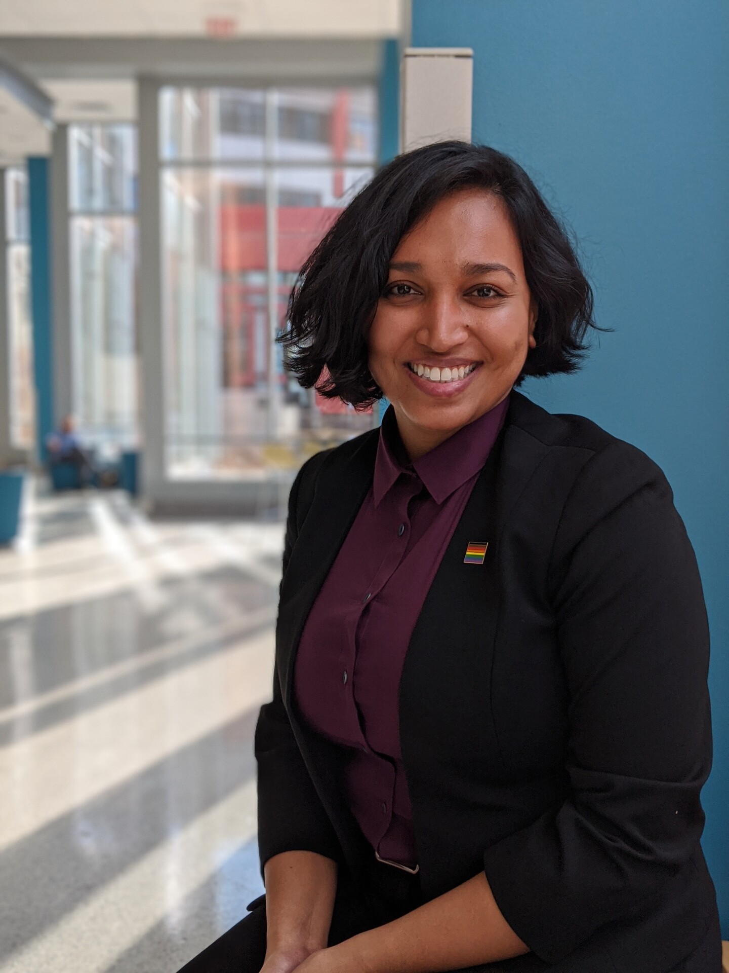 Smiling woman with a rainbow pin displayed on her lapel 