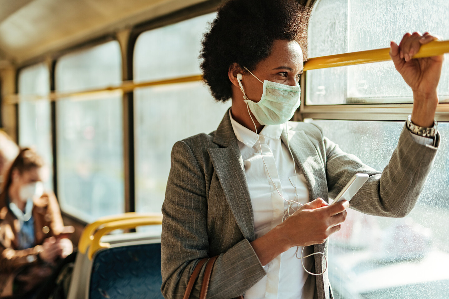 a person on public transportation wearing a mask while listening to music on a smartphone
