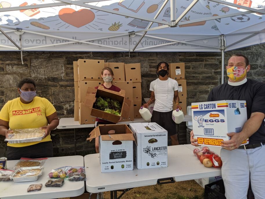 Four people wearing masks hold up groceries at a distribution center