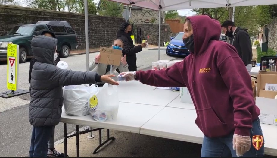 Children receive food from people working at a table wearing masks