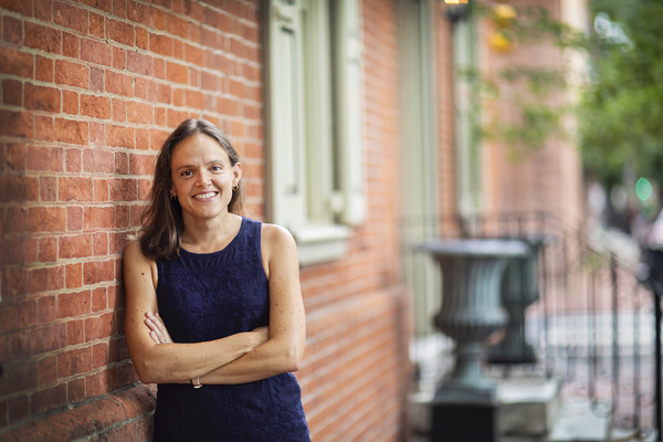 Person outside leaning on the wall of a brick rowhouse.