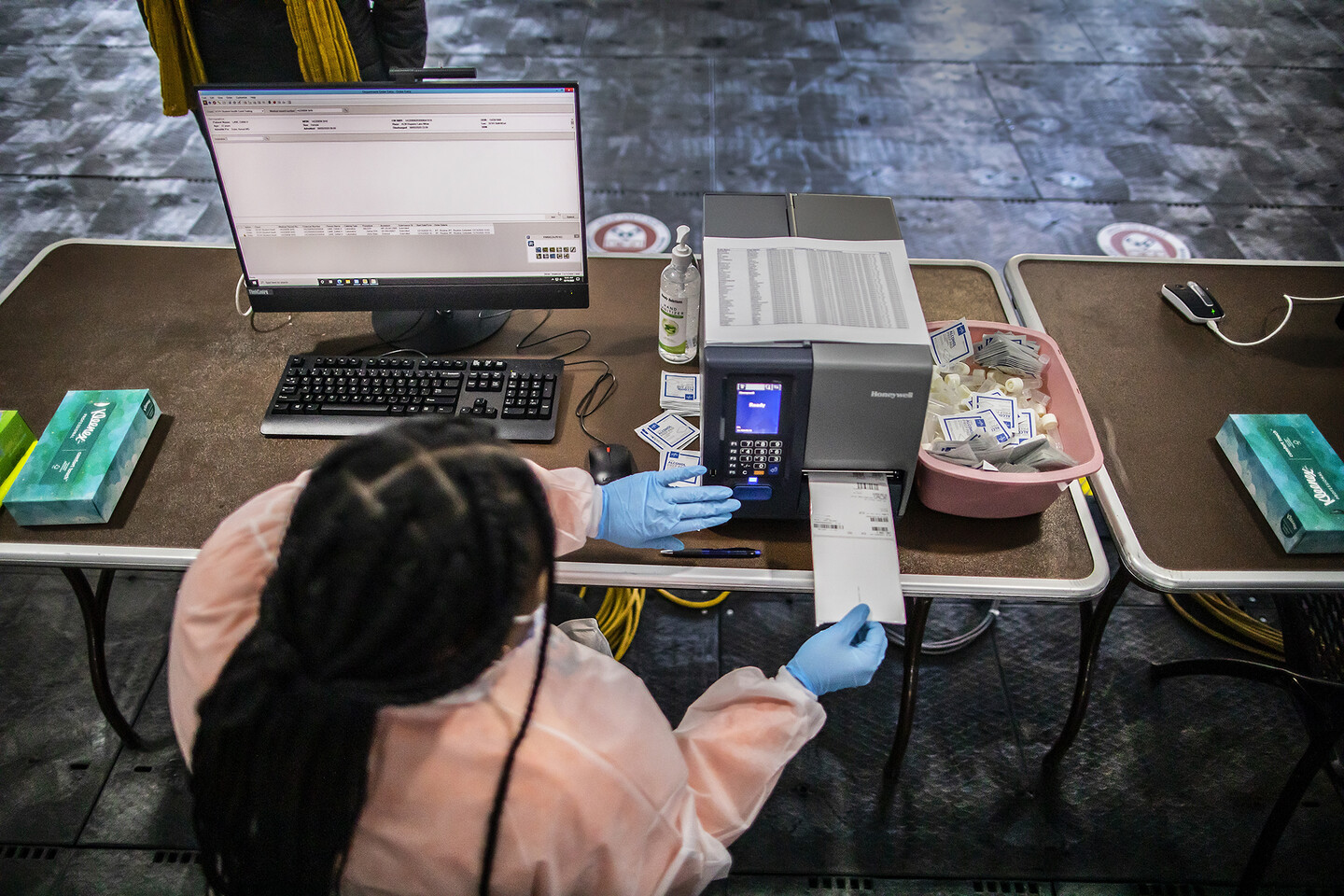 a person wearing a surgical gown and gloves taking out a piece of paper from a printer while working at a computer desk