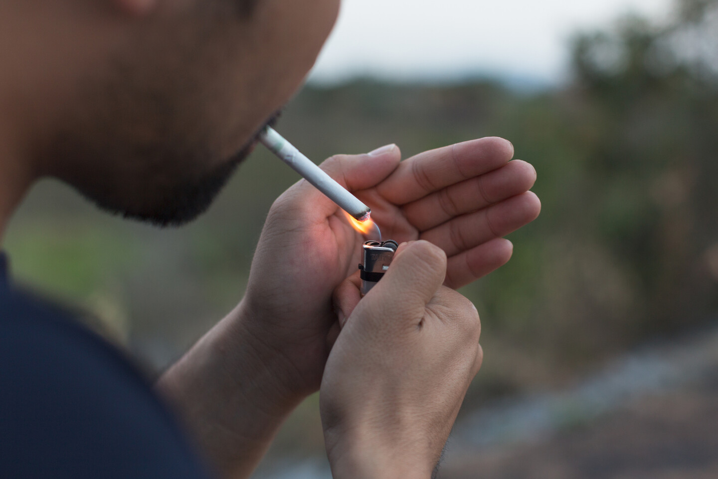 young person with beard lights a cigarette
