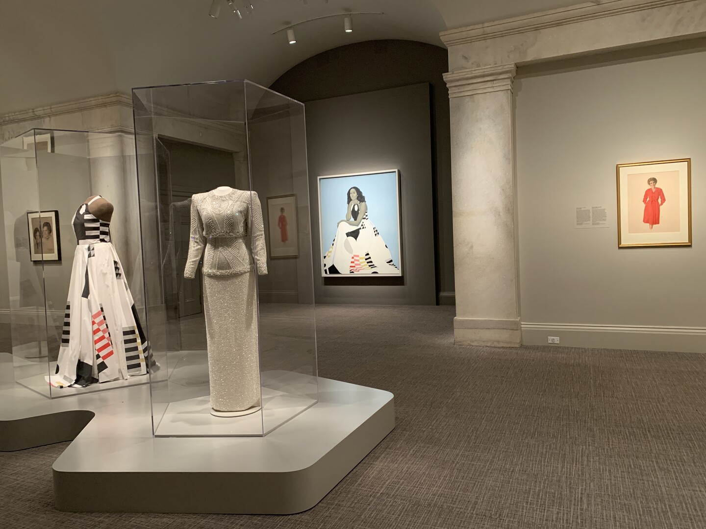 two dresses in glass cases and two portraits on the wall
