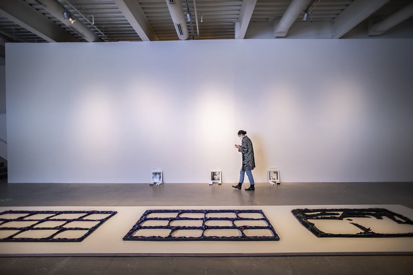 Artist walking through gallery with fabric works on floor and photos leaning against the wall