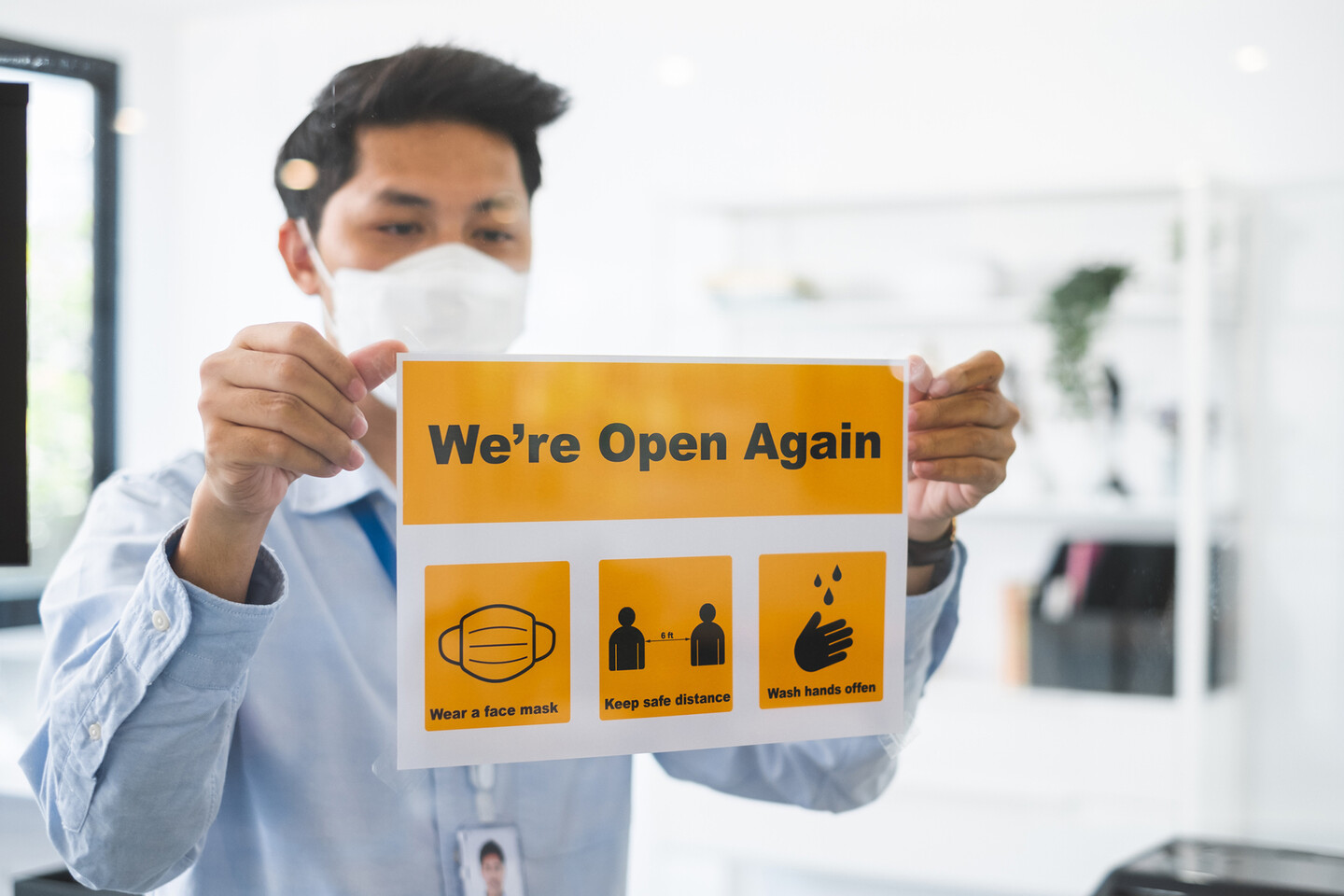 person putting up a sign in the window saying "we're open again"