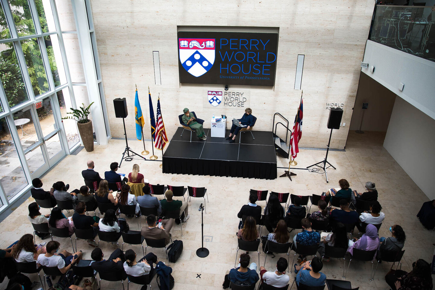 Former president of Liberia Ellen Johnson Sirleaf sits on a stage with NPR reporter Deborah Amos, with rows of onlookers in chairs and a sign behind them reading Perry World House