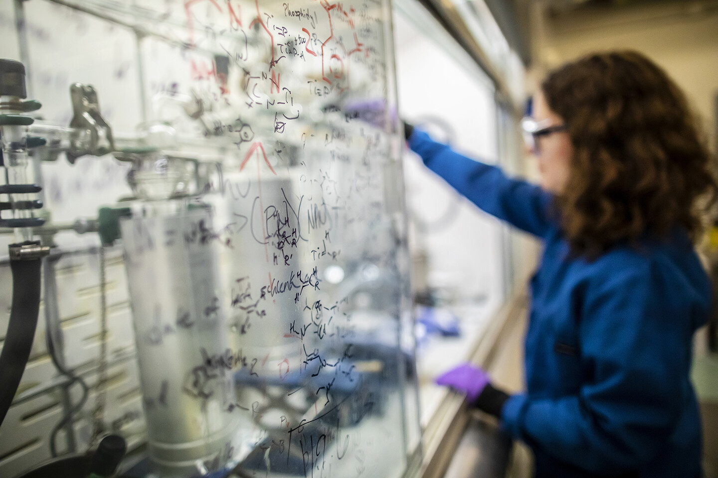 Scientist works in a ventilated hood in a chemistry lab with chemical formulas written on the plastic covering.