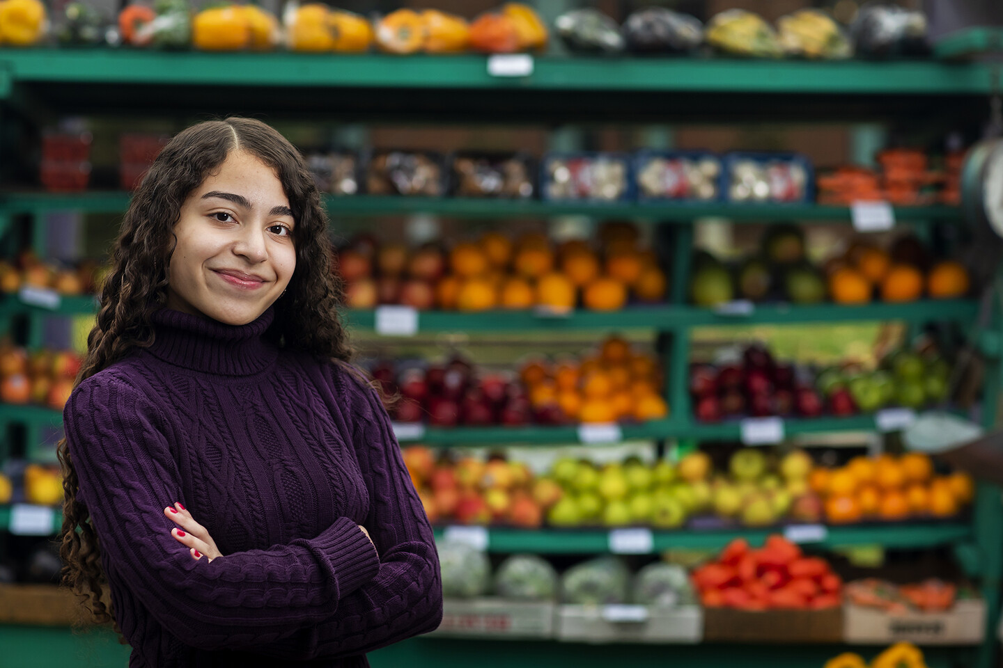 Dangela Fonseca stands in front of a fruit stand with arms crossed