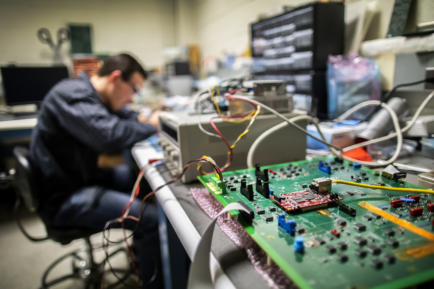 a person working in the background on a soldering iron with a chip in the foreground
