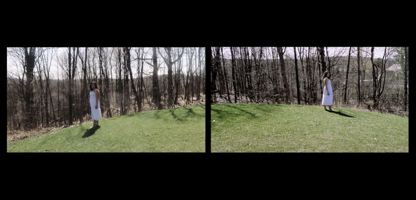 student standing outside on a hill of green grass with leafless trees behind