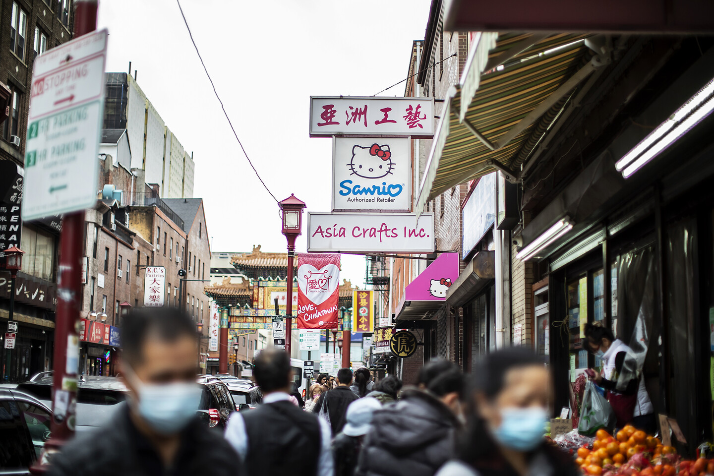 Image of a bustling street in Chinatown, with the red and gold Friendship Gate in the background. A shop sign reads "Sanrio, Asia crafts, Inc."