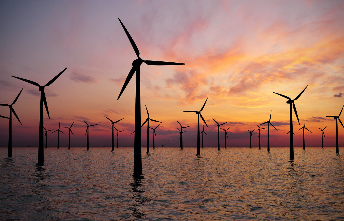 Wind turbines in water, with a sunset in the background. 