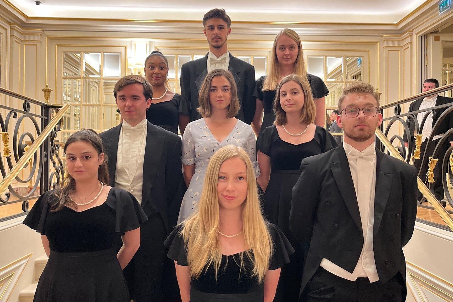 Nine members of the Penn Glee Club standing in an ornate stairway wearing formalwear