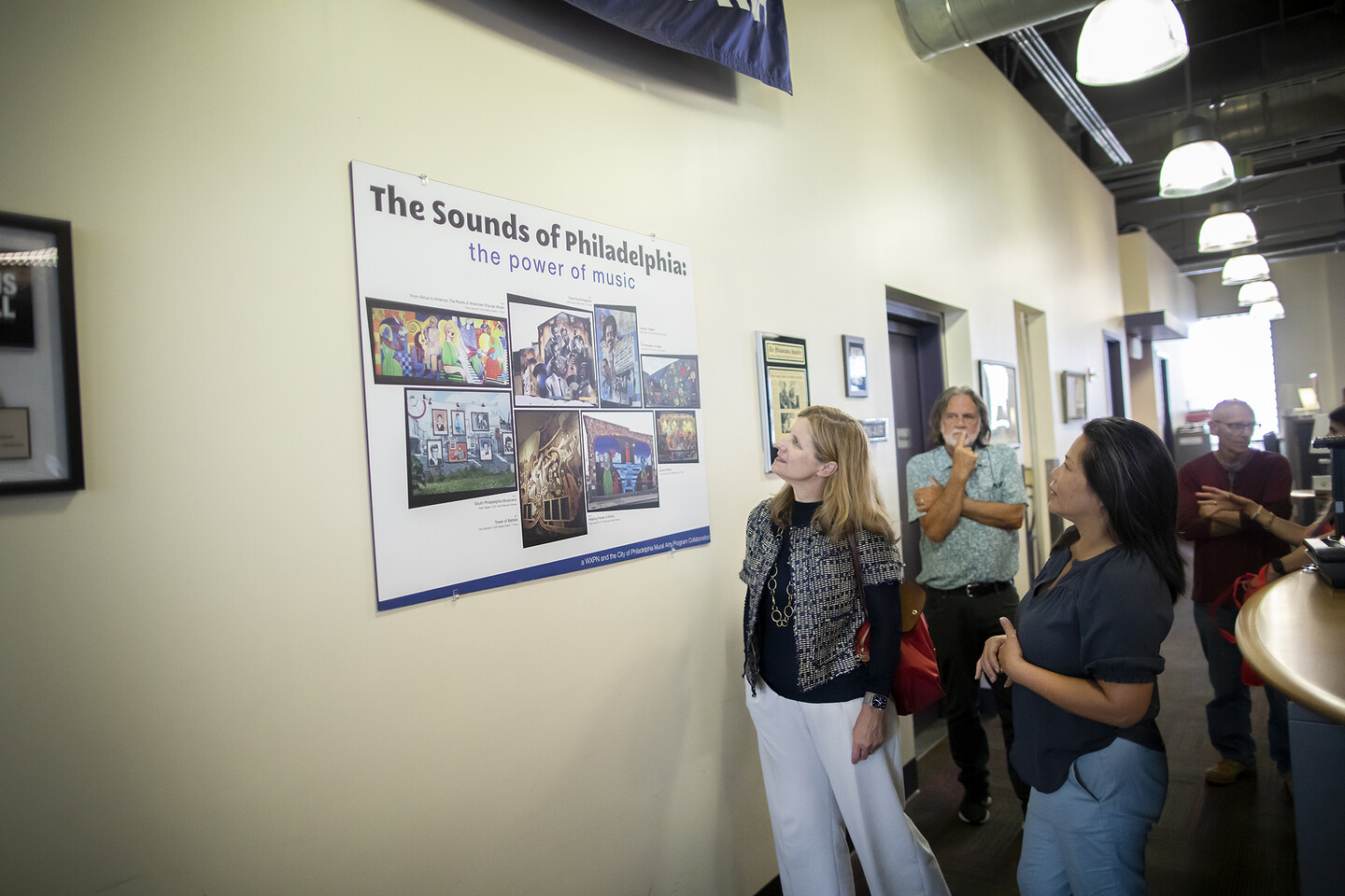 Penn President Liz Magill and XPN staff crowd around a poster that reads 'The Sounds of Philadelphia: the power of music"