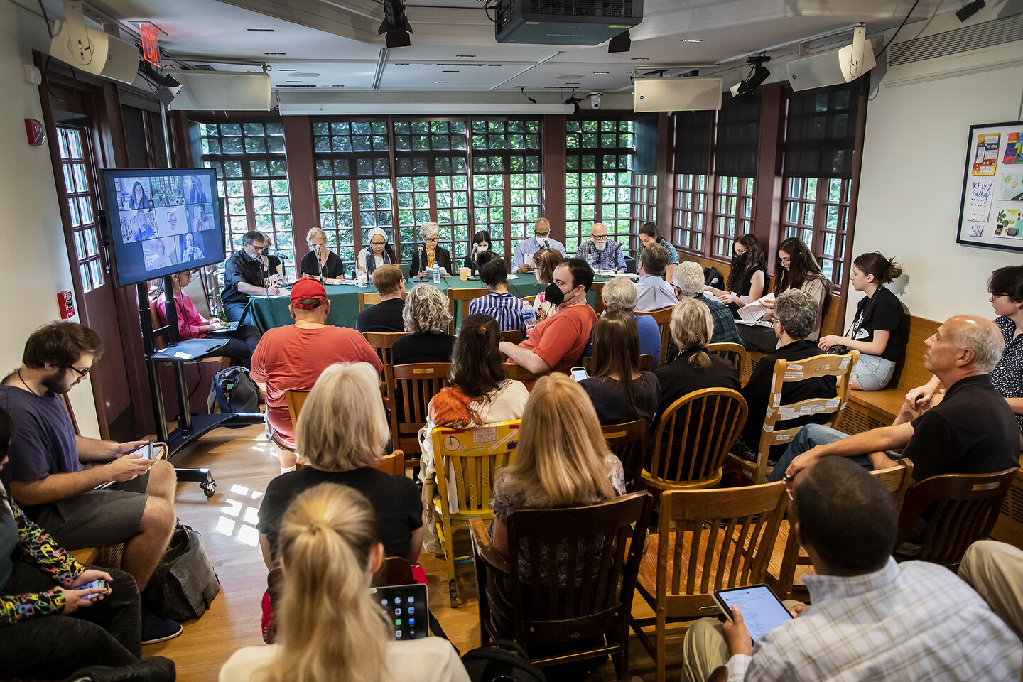 Kelly Writers House arts cafe filled with people sitting in chairs toward a long table with poets at the front with a wall of windows behind them 