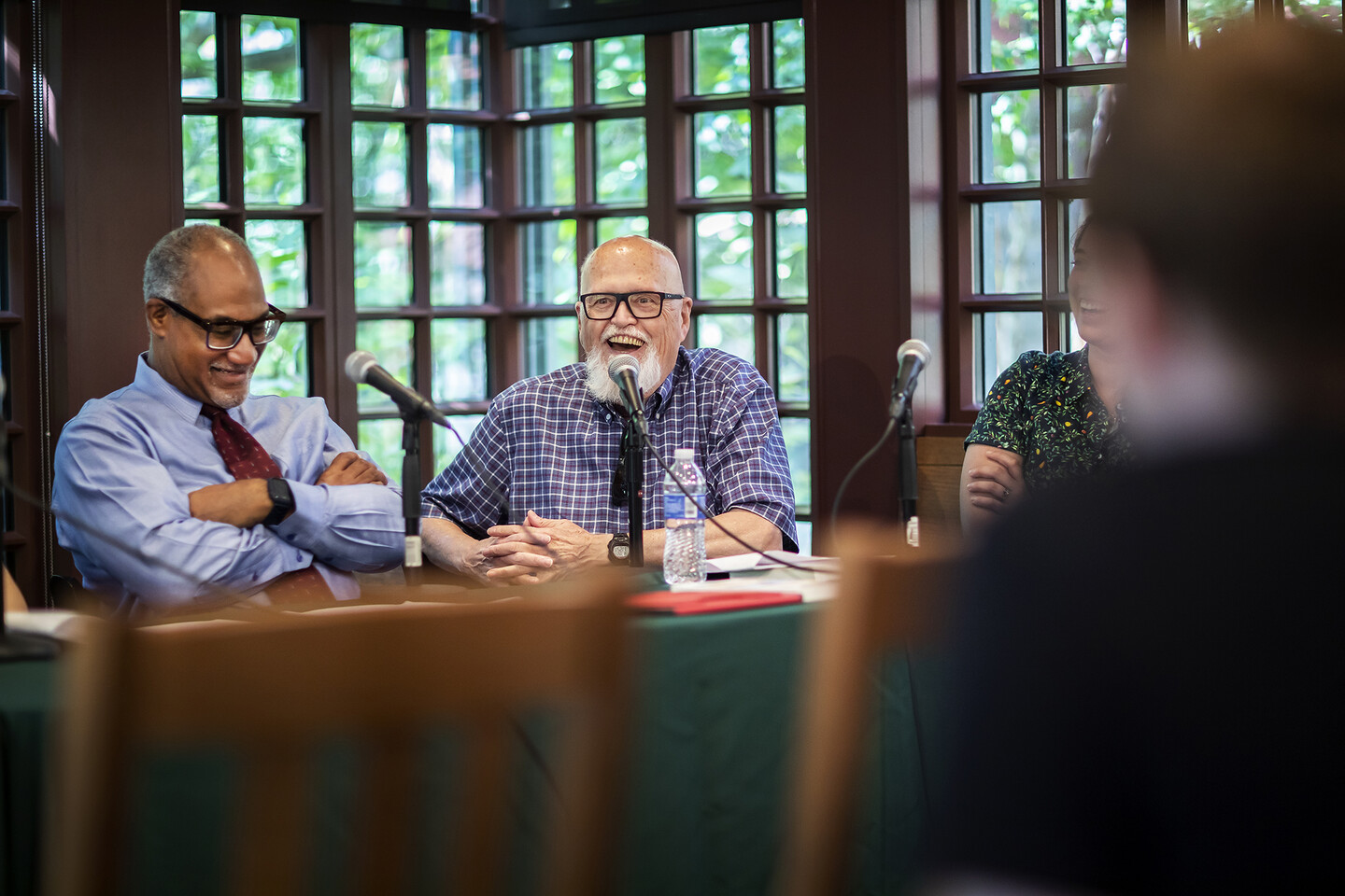 Ron Silliman sitting and speaking into a microphone while smiling, and Herman Beavers sitting next to him also smiling. 