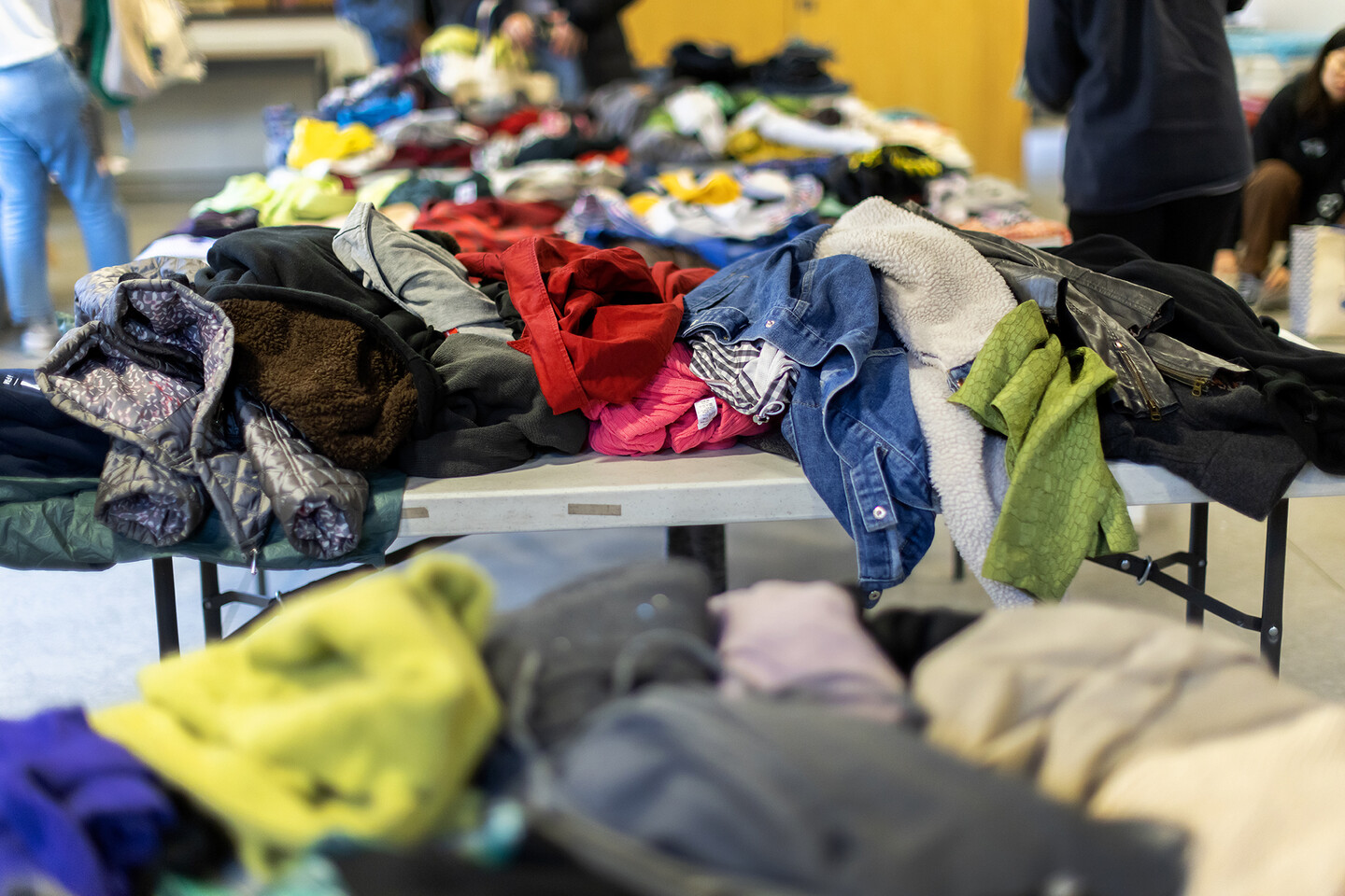 Piles of clothing on folding tables in the foreground, with students in the background