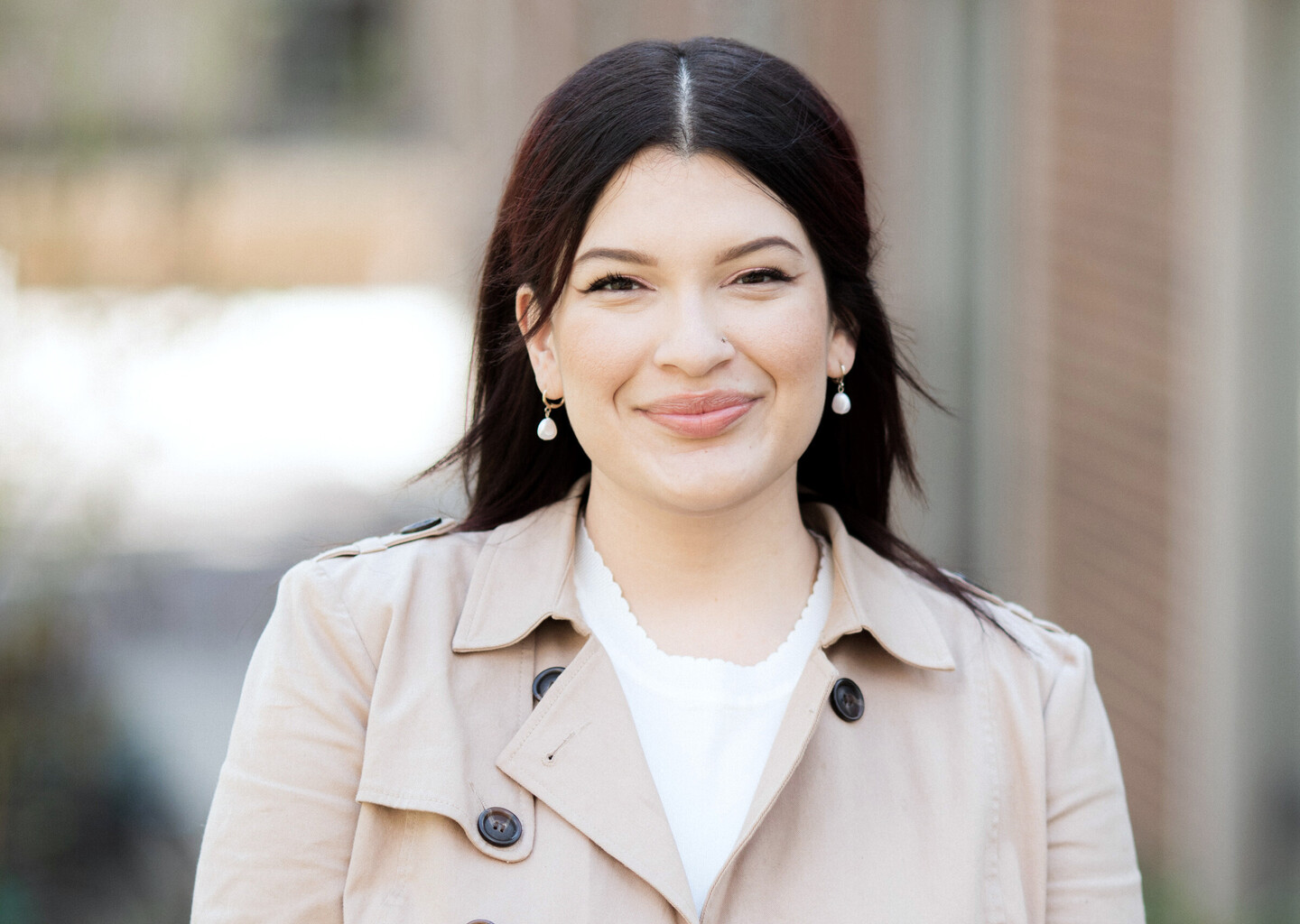 A woman in a trench coat smiles at the camera