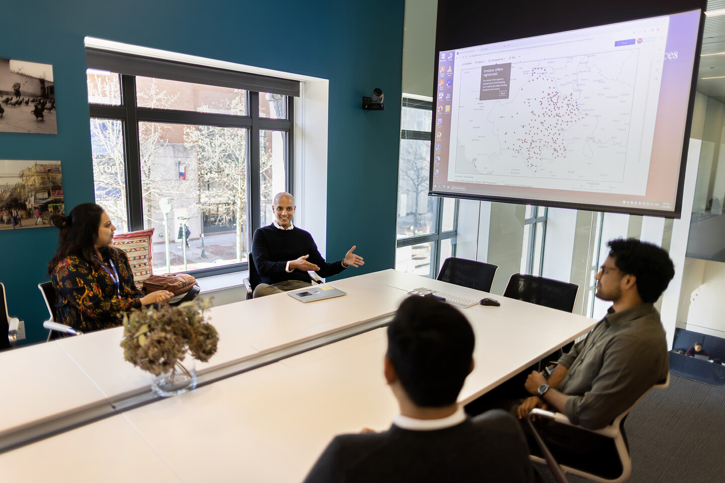 Four people seated at a table discussing a map of India on a projector.