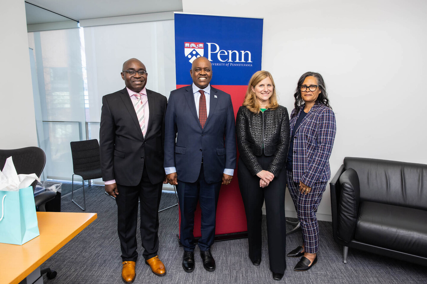 Four people stand next to each other in front of a sign reading Penn.