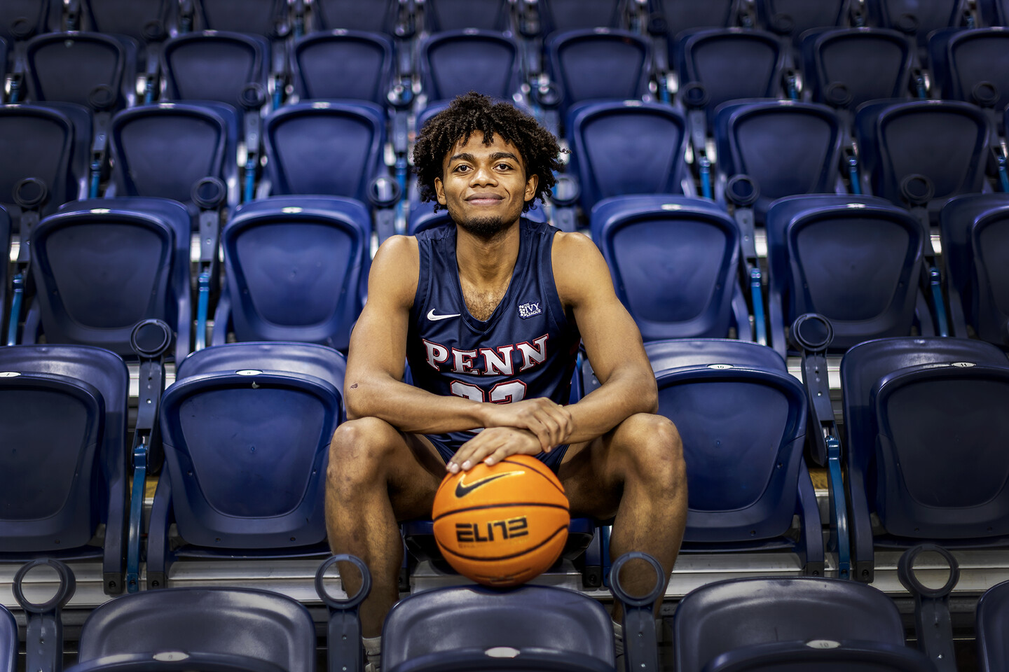 Monroe sits in the Palestra stands wearing his jersey and holding a ball.