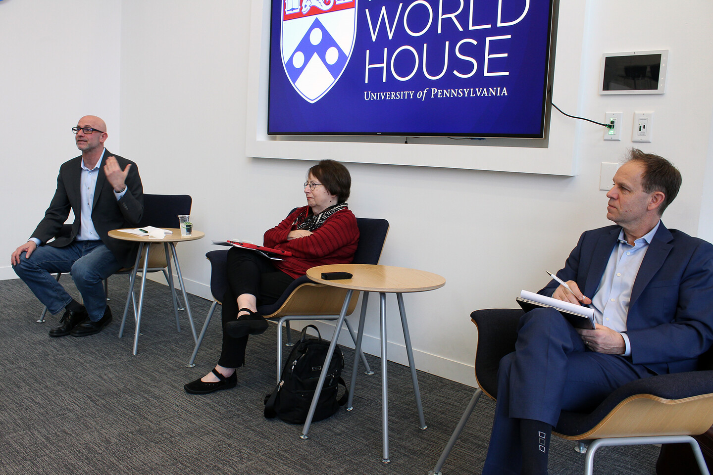 Three people sit in black chairs next to round wooden side tables at Perry World House.