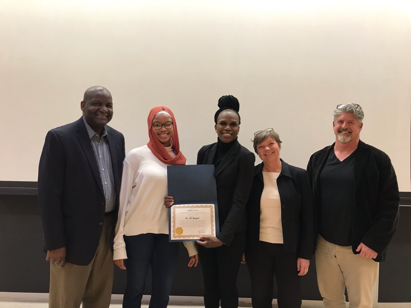 Five people pose holding a certificate