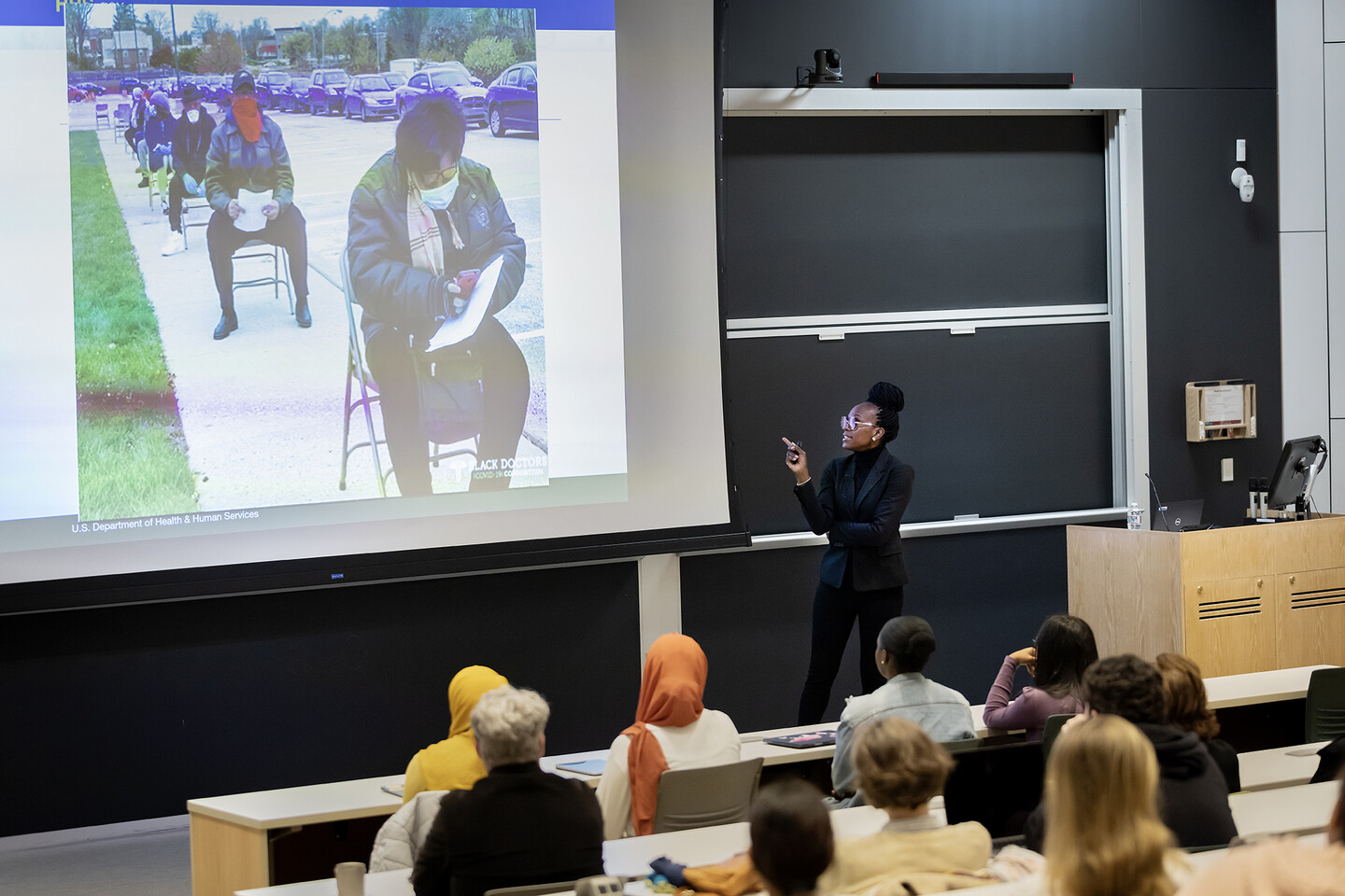 Speaker shows audience a slide of people sitting in a line on a sidewalk