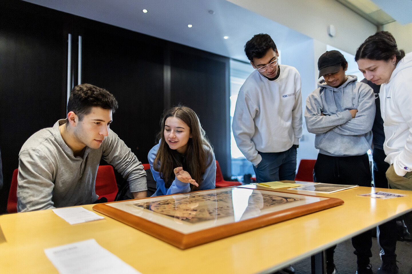 five students looking at printed materials while standing around a table