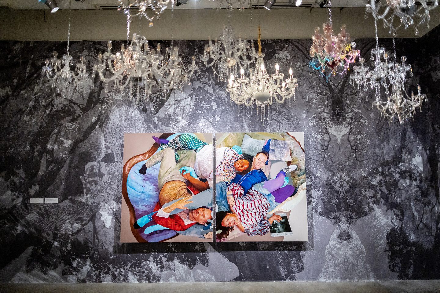 Portraits hung on muraled wall with chandeliers hanging above. 