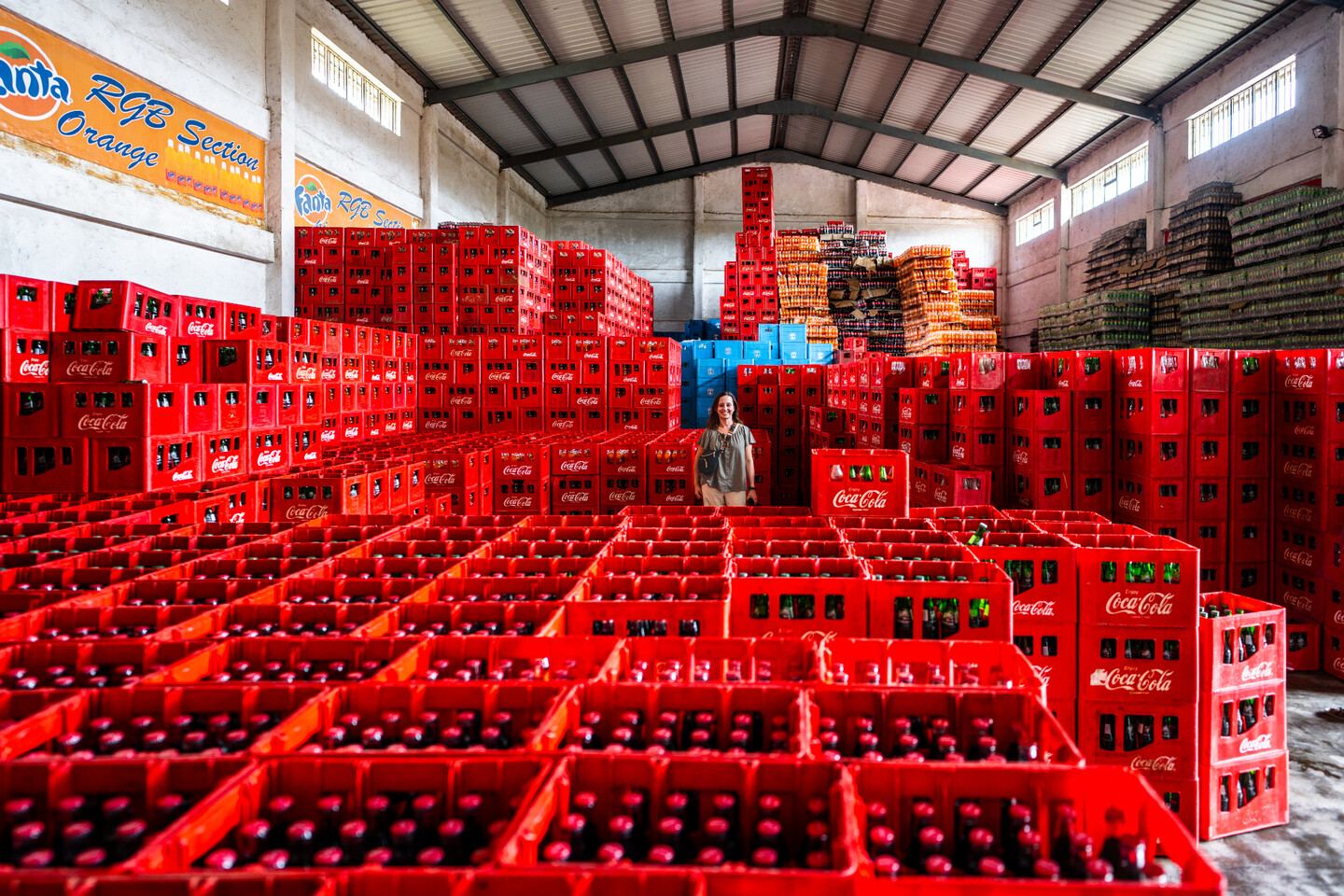 Sara Byala standing among hundreds of coca-cola bottle cartons. 