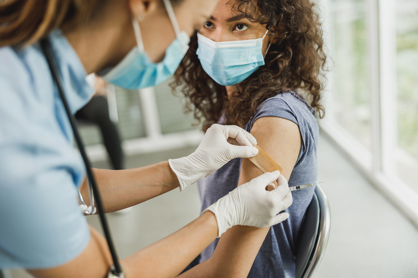 A medical professional puts a bandage on a teen’s arm after vaccination.
