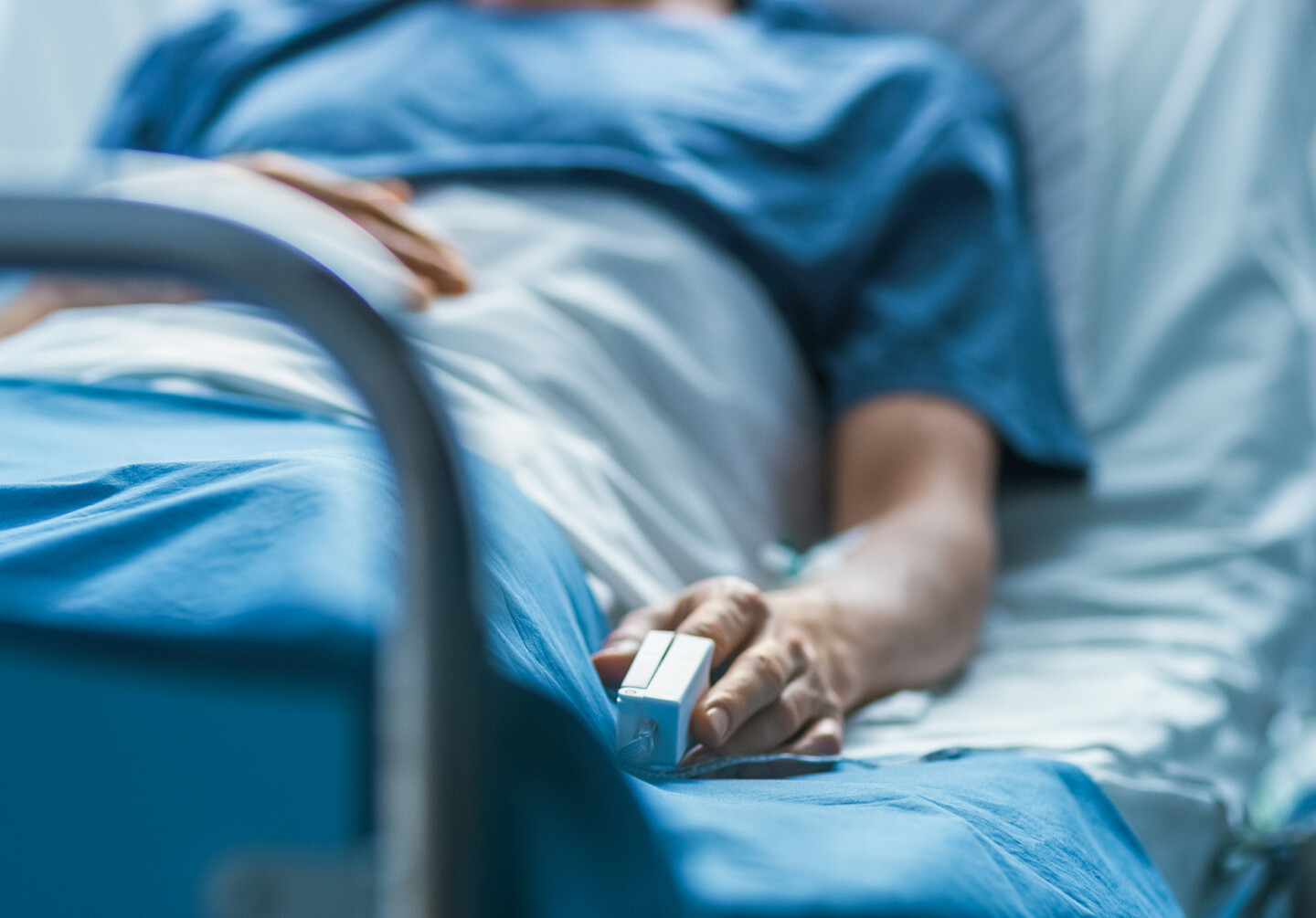 A patient in a hospital bed with an oxygen reader on their finger.