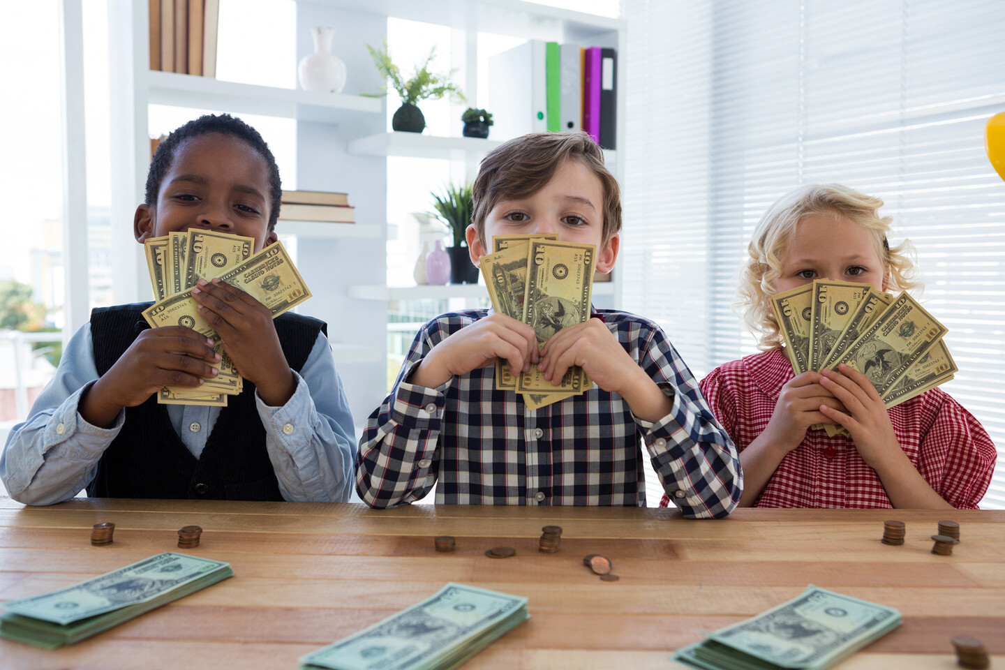 Three young children holding paper money seated at a table.