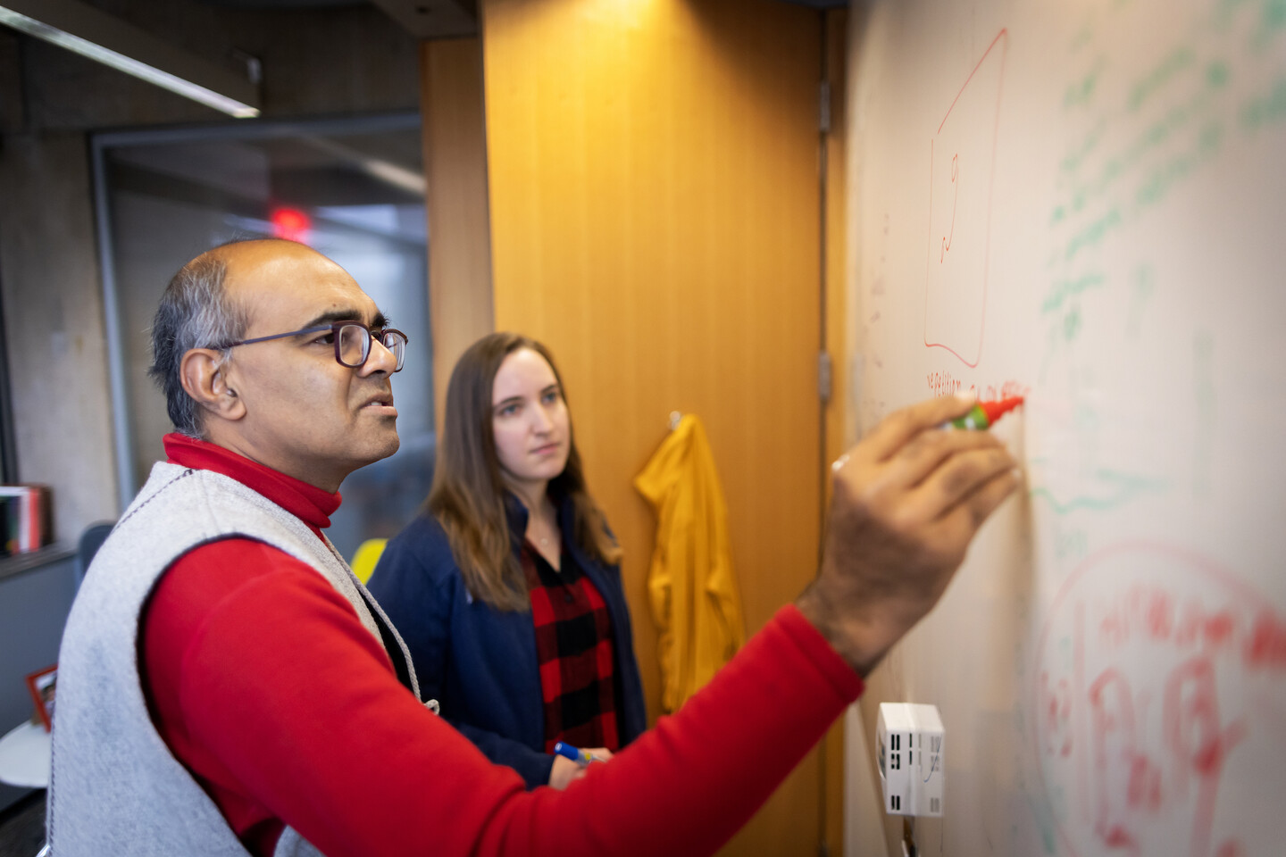 Vijay Balasubramanian writes equations on a whiteboard with a graduate student