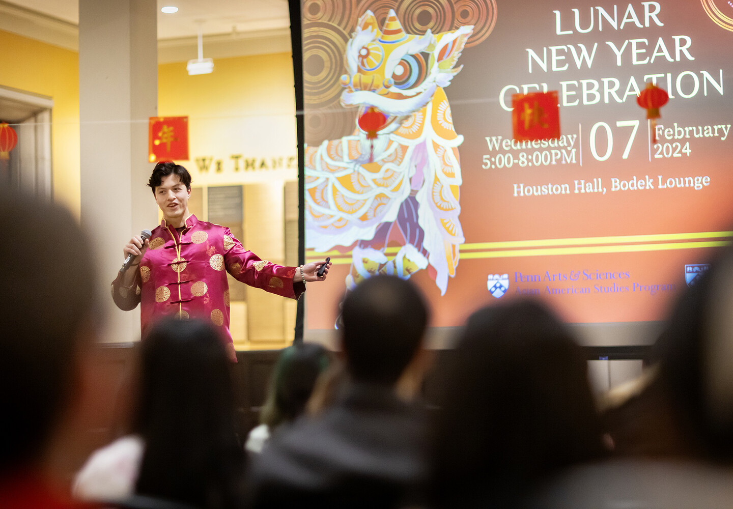Will Chan speaks at the Lunar New Year Celebration, Wednesday 5:00-8:00 p.m. on Feb. 7, 2024, in Houston Hall's Bodek Lounge. A screen behind Chan lists the event information