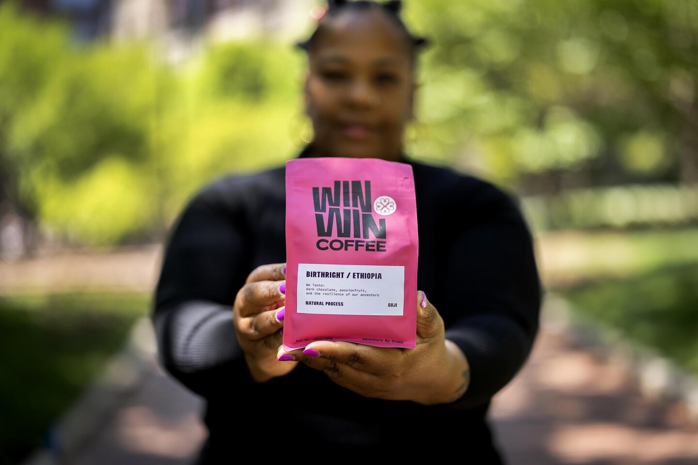 An image focused on a pink bag of coffee grinds. The bag is labeled Win Win Coffee and notes the product is from Ethiopia. Nikisha Bailey is holding the bag and is blurred in the background.