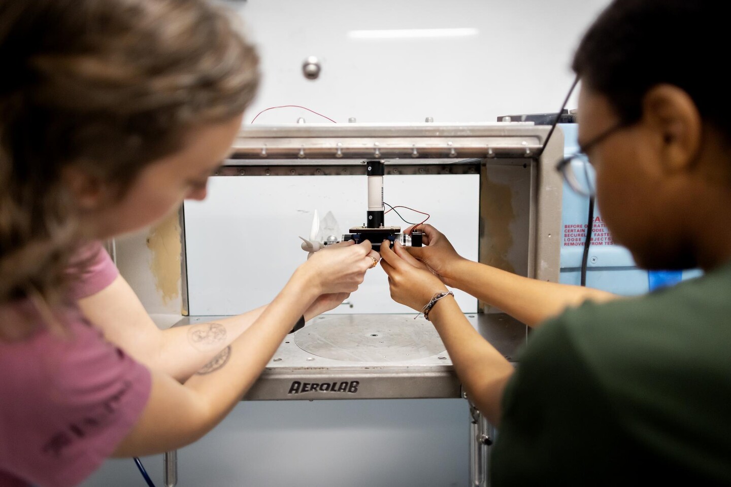 Lorena Grundy and Ngaatendwe Manyika hold a tiny wind turbin inside a wind tunnel.