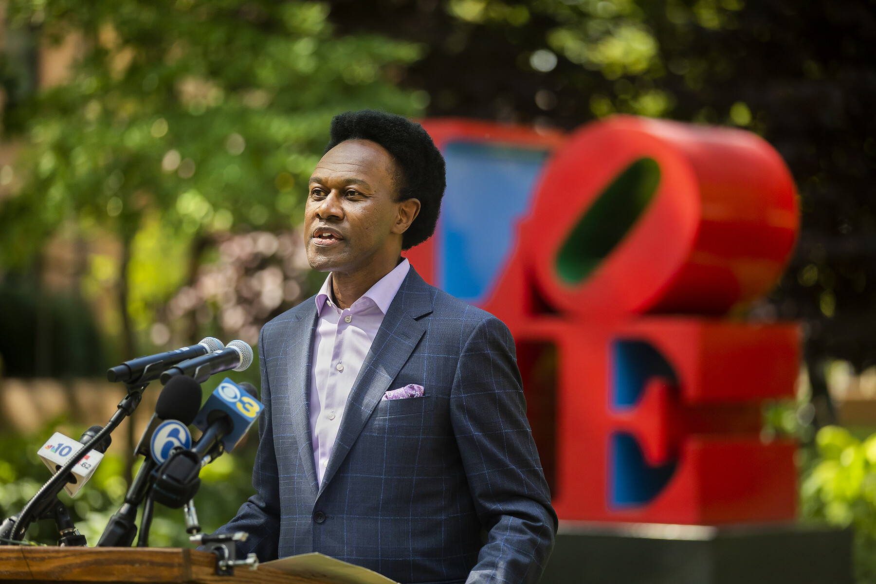Reverend Gipson speaking at a podium in front of the LOVE statue on Penn’s campus.